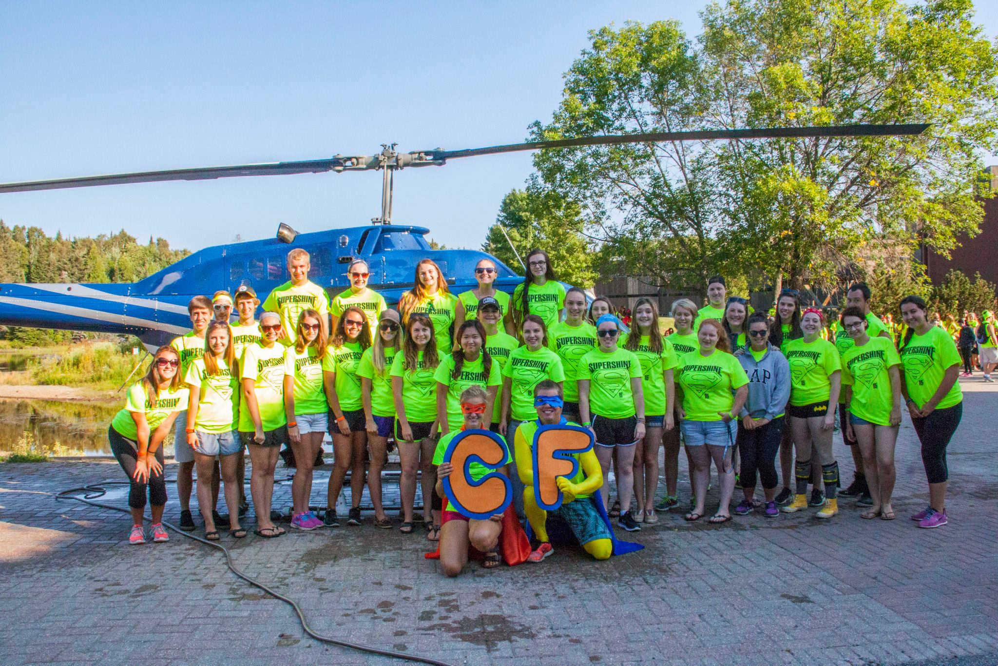 Group photo of students who did fundraising for Shinerama. Each student is wearing a bright yellow t shirt and they are posing in front of a parked helicopter.