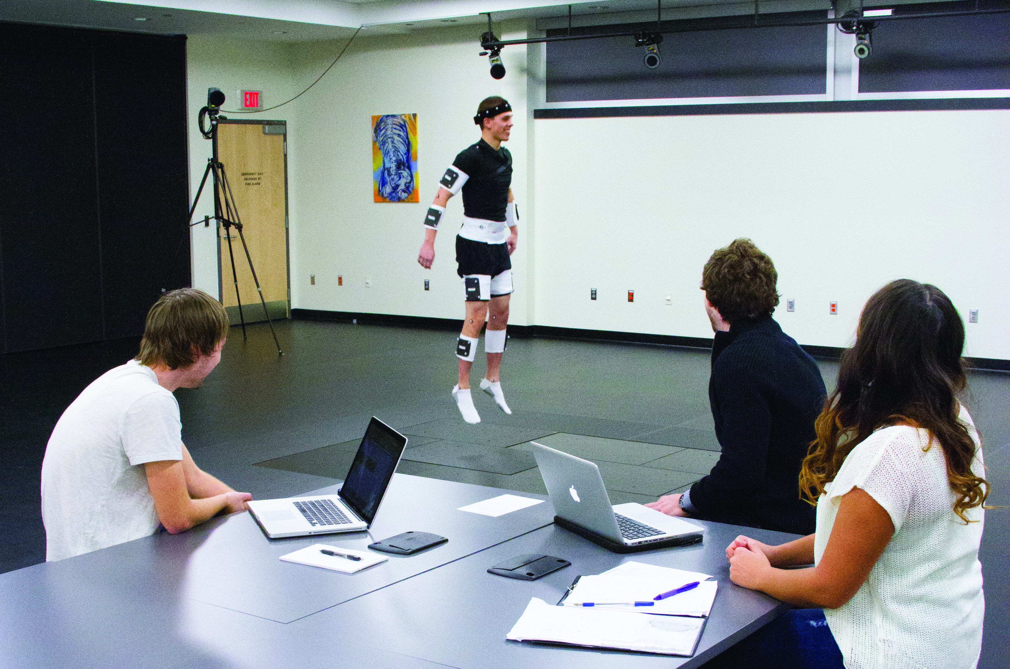 A student jumping with gears attached while 3 other students observe him
