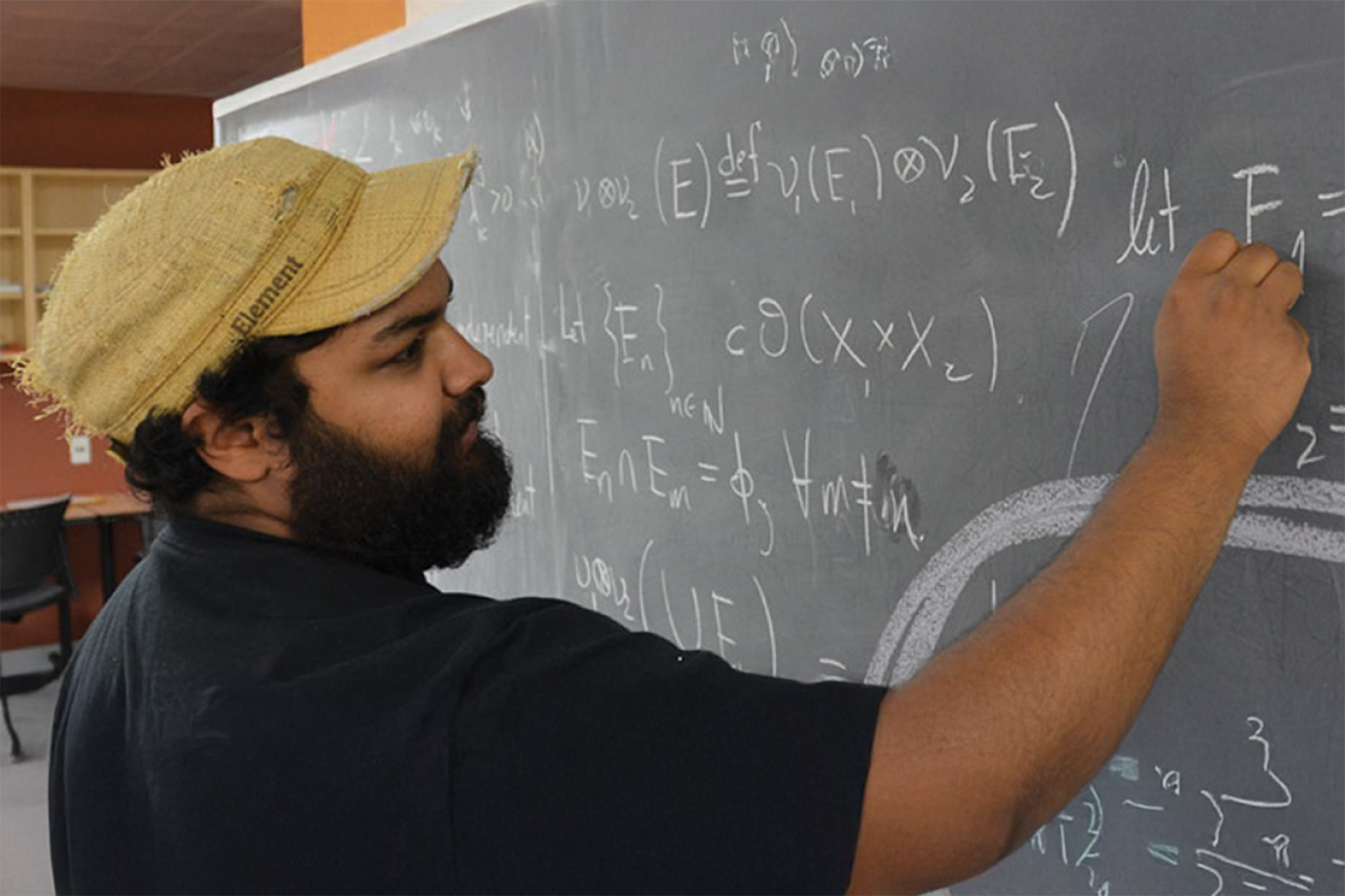 A student in black t-shirt writing math equations on the blackboard
