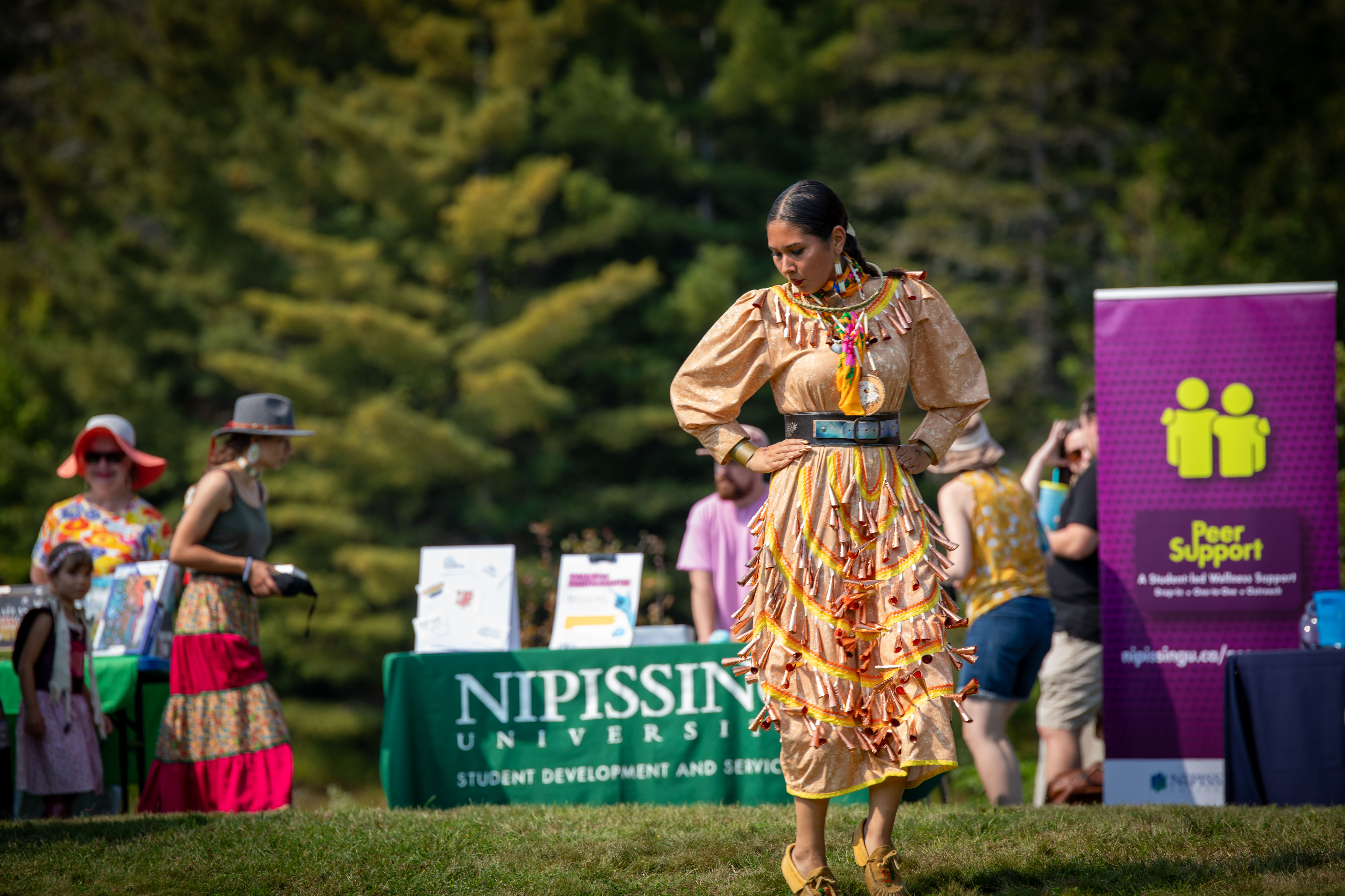 Pow wow dancer in yellow regalia beside the campus pond.