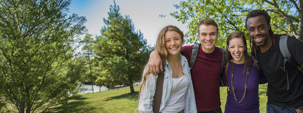 4 students looking into the camera with trees and greenery in the background