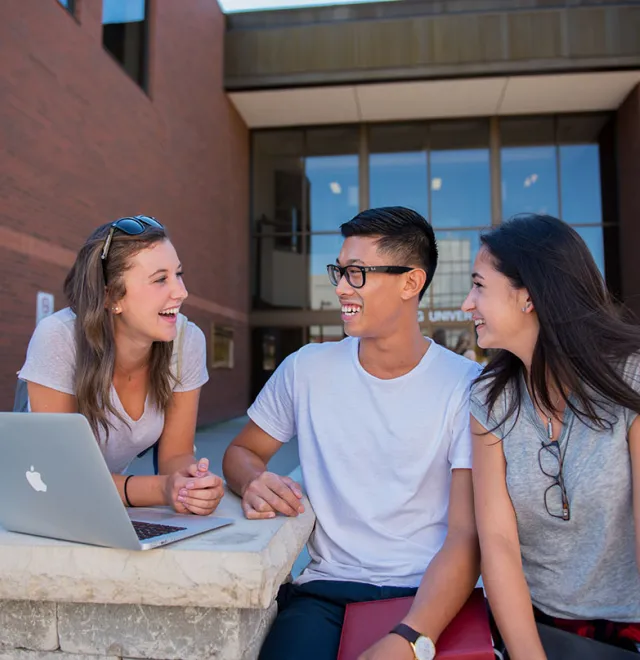 Three students sit on bench outside the front entrance to Nipissing University.