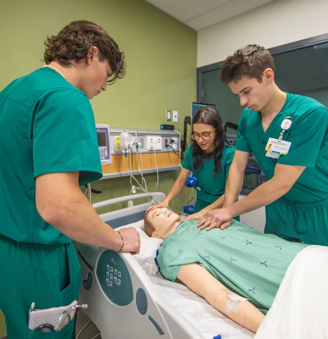 3 students in green scrubs doing chest compression on a mannequin in the simulation lab at Nipissing