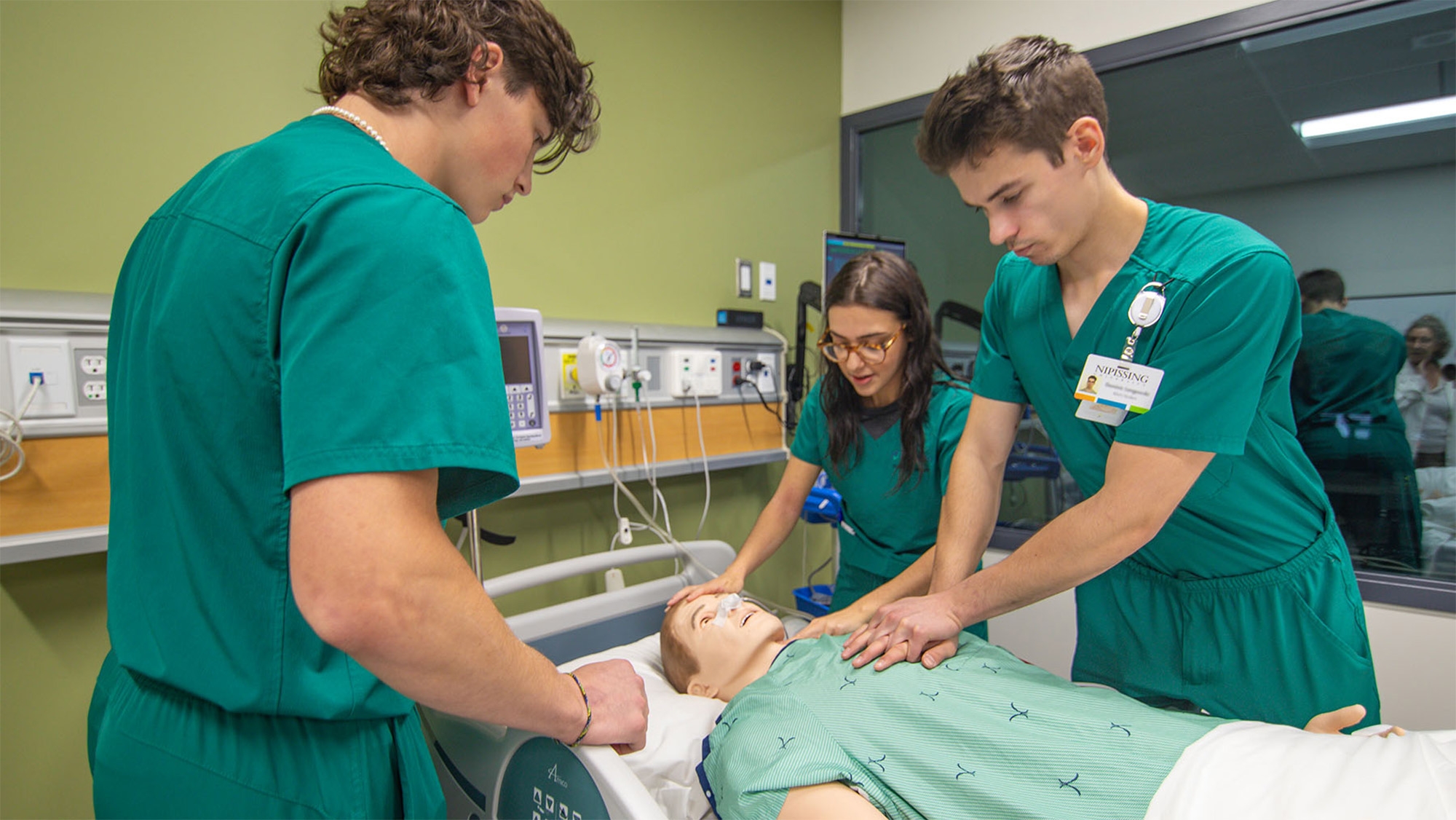 3 students in green scrubs doing chest compressions in the simulation lab at Nipissing