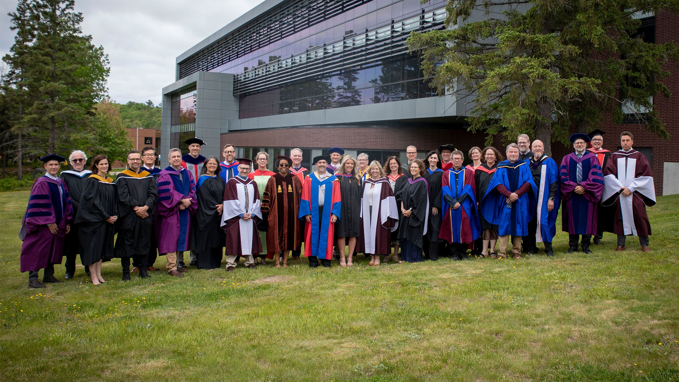 The entire Nipissing faculty of arts and science in convocation gowns standing in a group in front of the library background