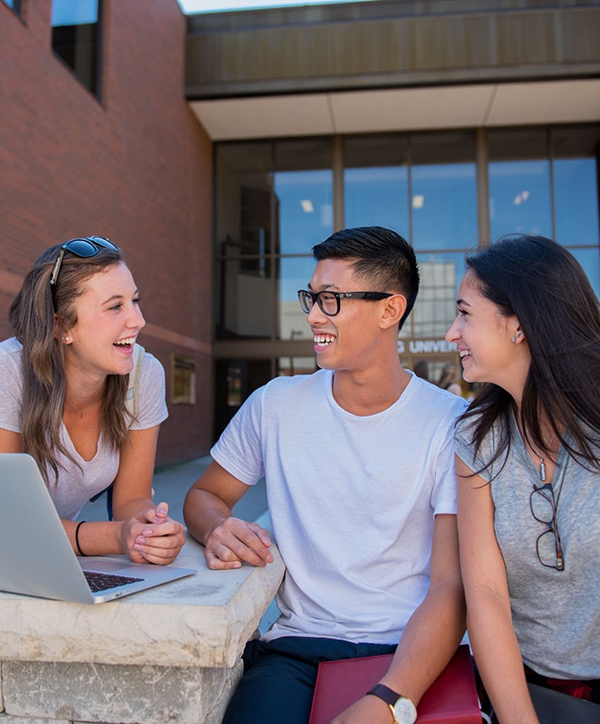 Three students sit on bench outside the front entrance to Nipissing University.