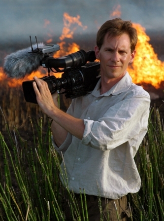Photo of a man with a video camera with fire behind him