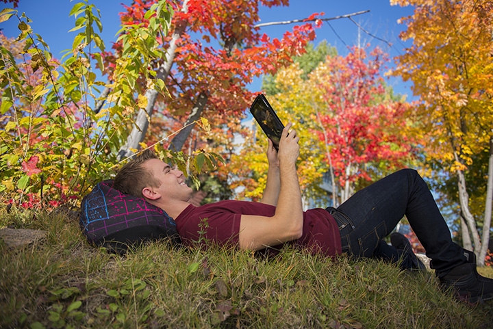 Photo of a student chilling with a tablet on the grass among beautiful fall colours