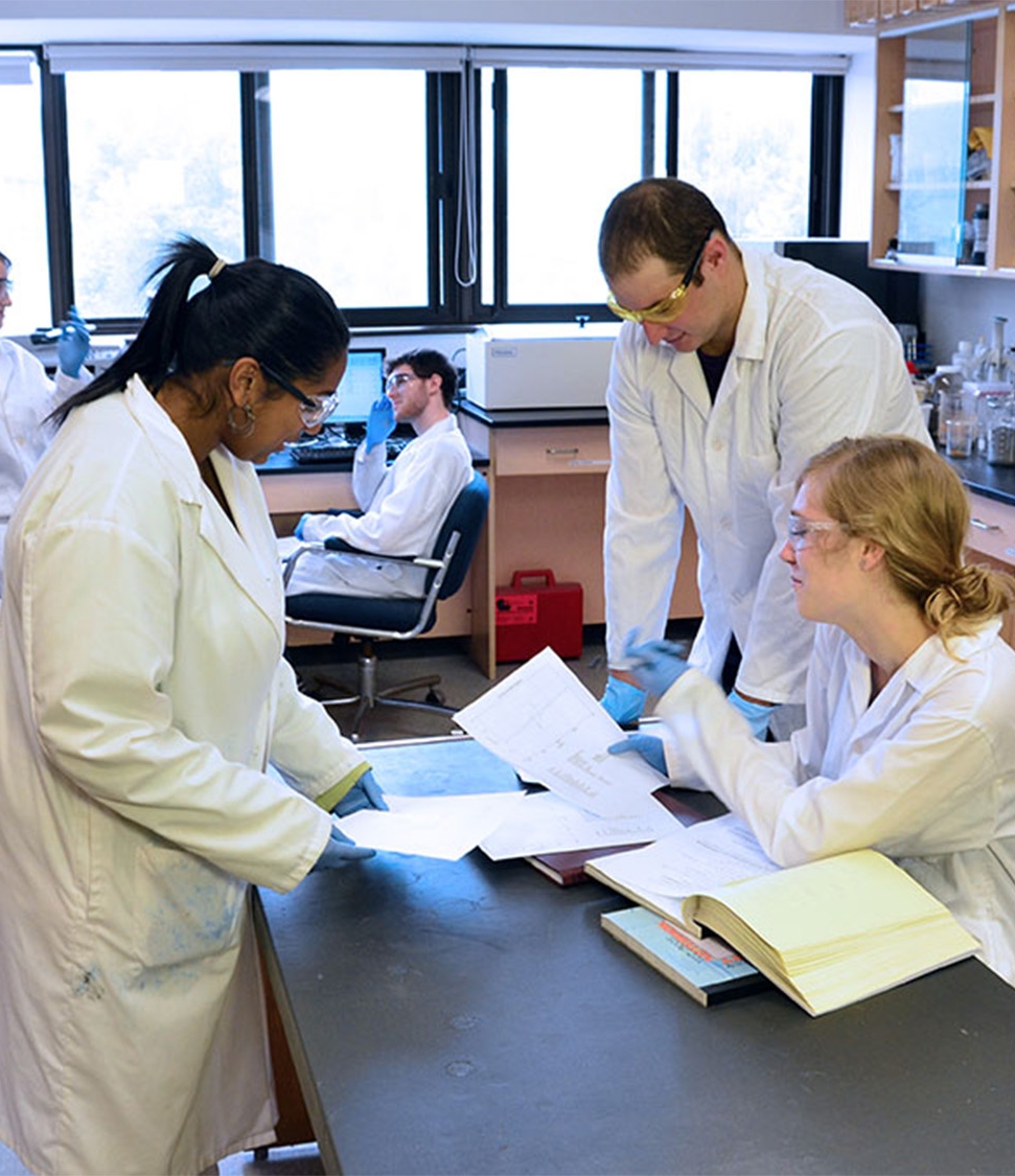 3 students in lab coats working on an island in the middle of the science lab