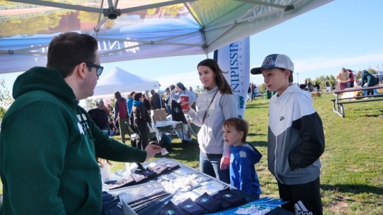 A family of 3 at Nipissing University pop up shop during NU Homecoming 2025
