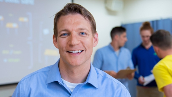 Professor in blue shirt in the foreground with a group in the background