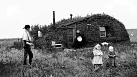 A black and white picture of a farmer family standing near their house in the fields