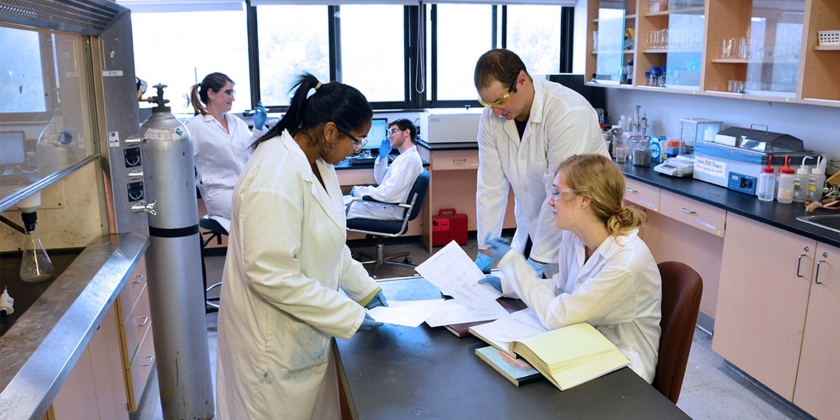 3 students in lab coats working on an island in the middle of the science lab