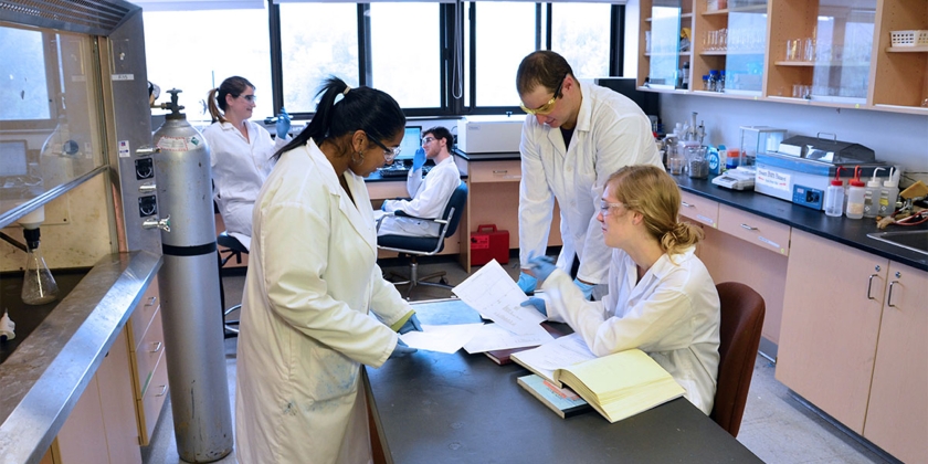3 students in lab coats working on an island in the middle of the science lab