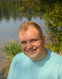 A man in light blue t-shirt against a water background