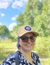 A woman wearing a cap taking a picture against a nature background