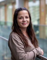 Pamela Forest, Dibaadan Wellness Coordinator smiling warmly in the library.