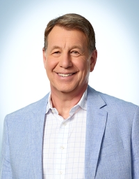 A man in light blue blazer against a light background with blue corner vignette
