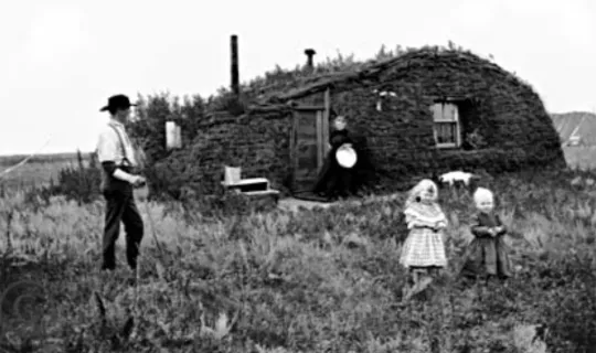 A black and white picture of a farmer family standing near their house in the fields
