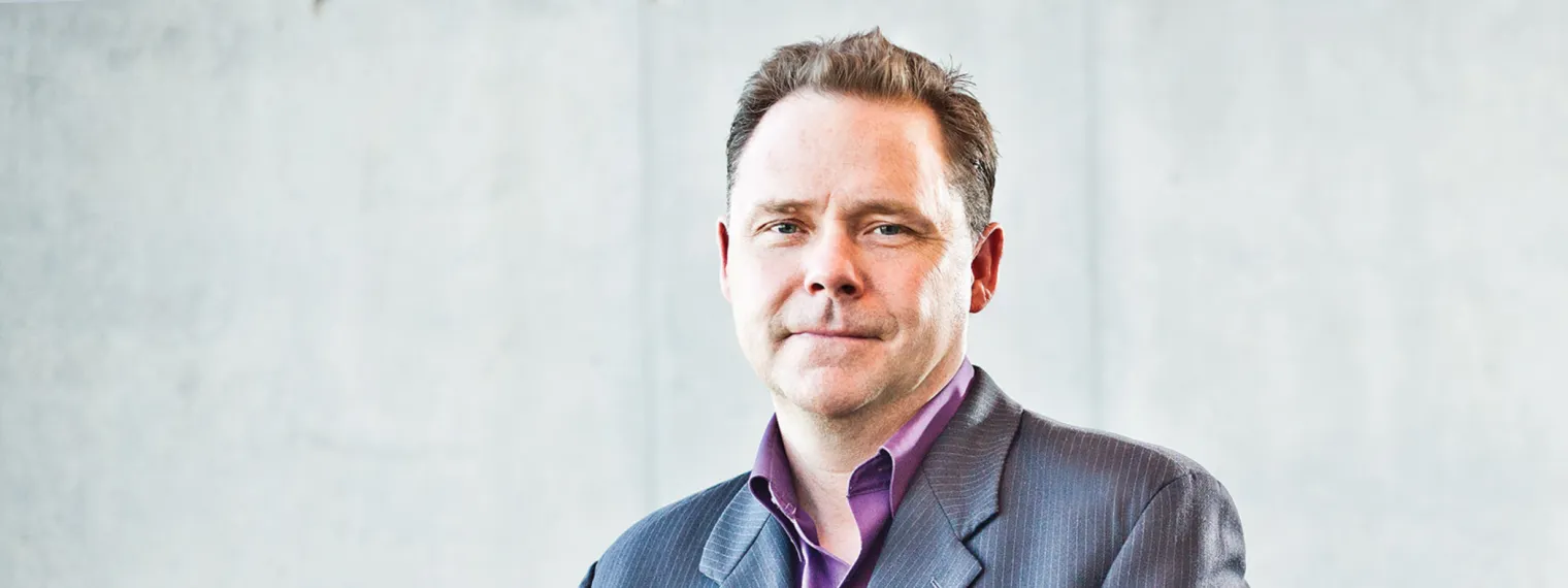 Dr. Glen Sharpe sitting in front of a light neutral background. 