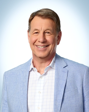 A man in light blue blazer against a light background with blue corner vignette