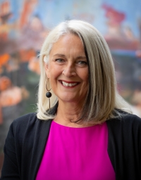A woman in pink and black top in front of a colorful background