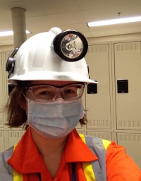Wearing a bright orange safety suit, white hard hat with cap lamp, mask, and safety glasses