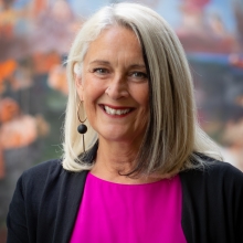 A woman in pink and black top in front of a colorful background